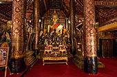 Wat Xieng Thong temple in Luang Prabang, Laos.  The main Buddha of the sim sits on a platform, surrounded by smaller statues, candles, and offerings. 